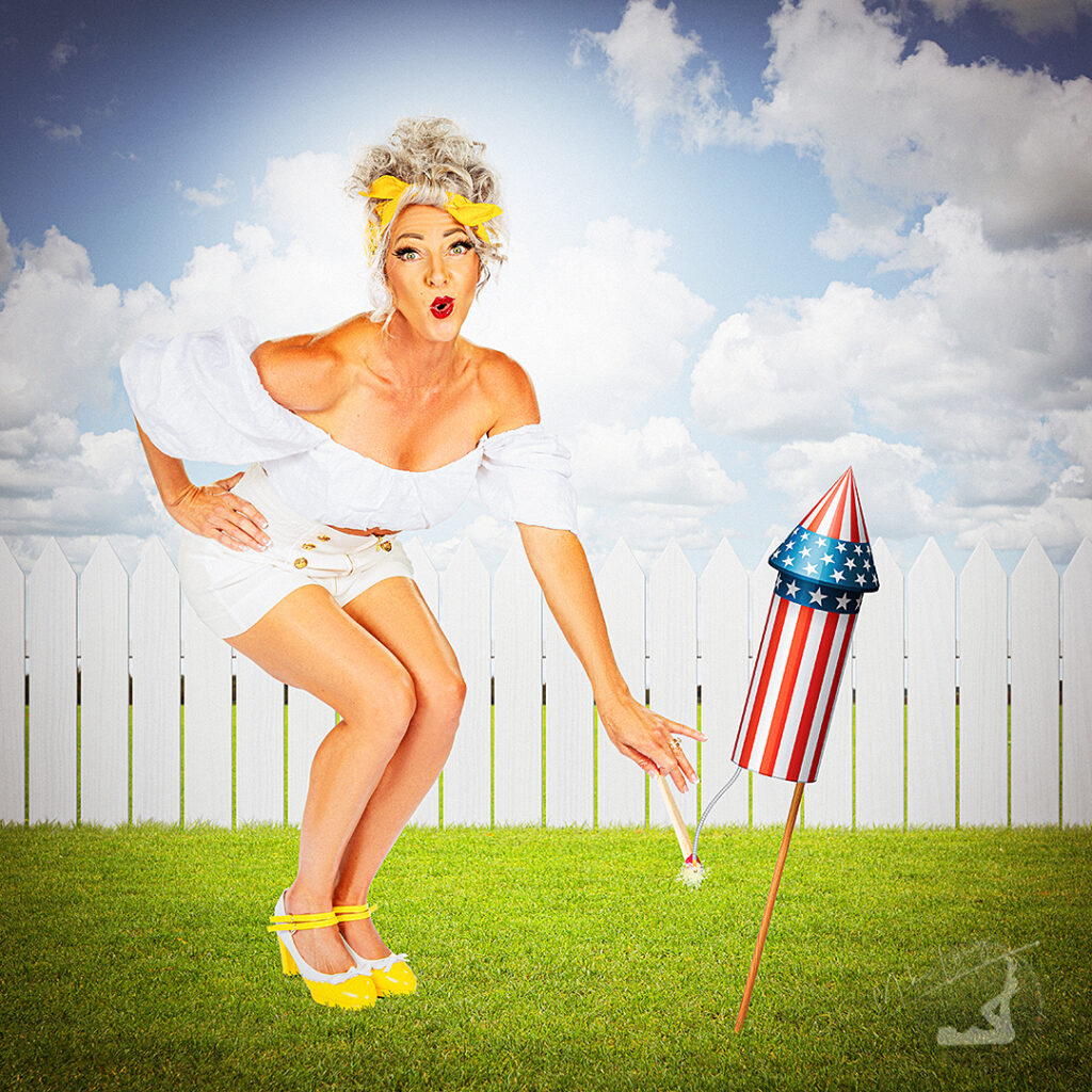 Woman in vintage outfit lighting a large patriotic firework in a grassy yard, with a white picket fence and cloudy sky in the background.
