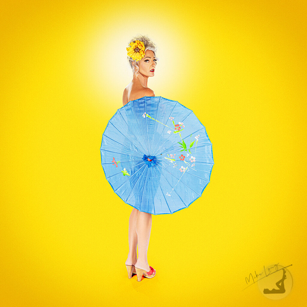 Woman with a flower in her hair holding a blue parasol, standing against a bright yellow background.