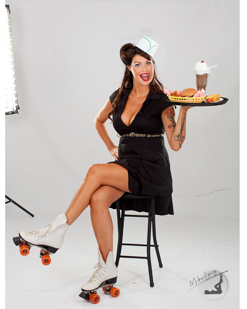 Woman in retro waitress outfit with roller skates, sitting on a stool, holding a tray with a burger, fries, hot dog, and milkshake.